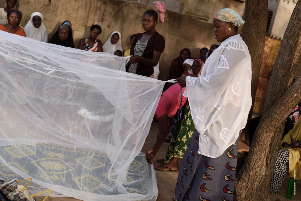 In December 2017, a photographic reportage, commissioned by an Italian NGO, took me to travel to Burkina Faso. The NGO has been operating for several years in the sub-Saharan country with projects aimed at containing malaria, which is endemic among the Burkinabé population. In these two images we see some women teaching other women how to prevent contagion caused by the Anopheles mosquito, carrier of the disease. In their demonstration, these women illustrate how to use mosquito nets to avoid being affected by the infection.
